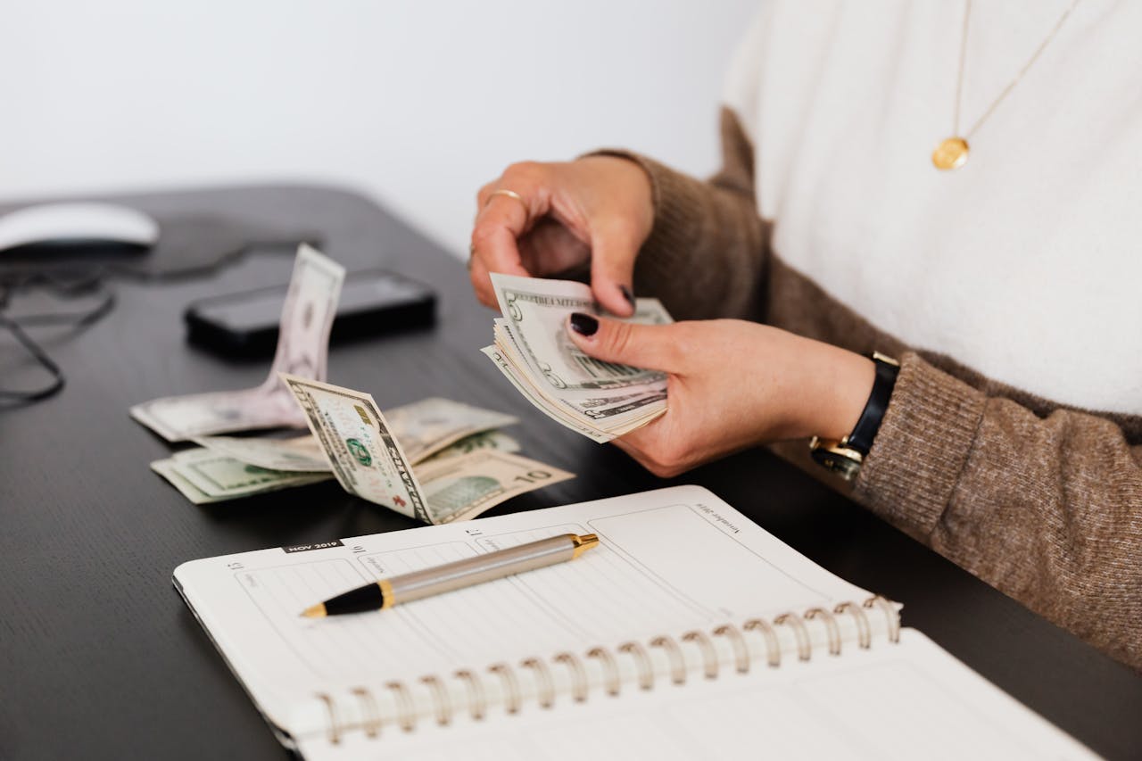 our-story Close-up of person counting cash with notepad on desk, indicating financial tasks.
